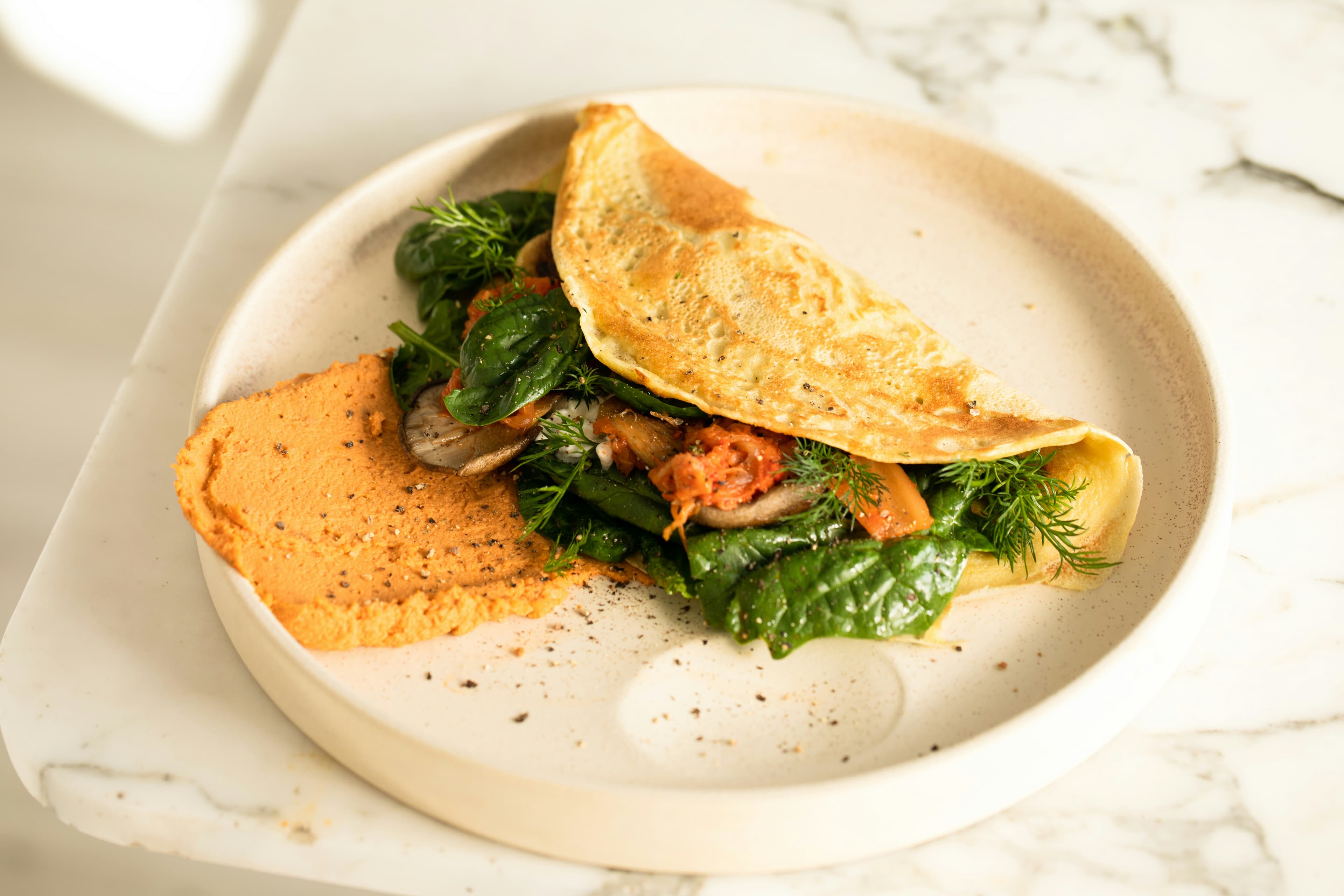 A white plate topped with an omelet and greens